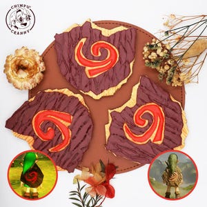 Puede incluir: Tres galletas con forma de escudo con glaseado morado oscuro y un diseño de espiral rojo brillante. Las galletas tienen una superficie texturizada y están dispuestas sobre una alfombrilla redonda de cuero marrón. Dos recuadros muestran.