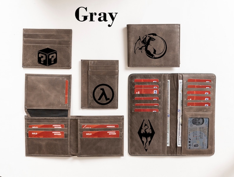 May include: A set of five gray leather wallets with different designs. The wallets feature a question mark in a box, a lambda symbol, a dragon, and a dragon with a shield. The wallets are all closed and laid out on a white surface.