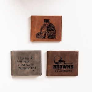 May include: Three different leather wallets with personalized engravings. The first wallet has a photo of a father and son. The second wallet has the text "i love this life with you I love you to the moon & back XO". The third wallet has a football helmet and the text "BROWNS *Cleveland*".