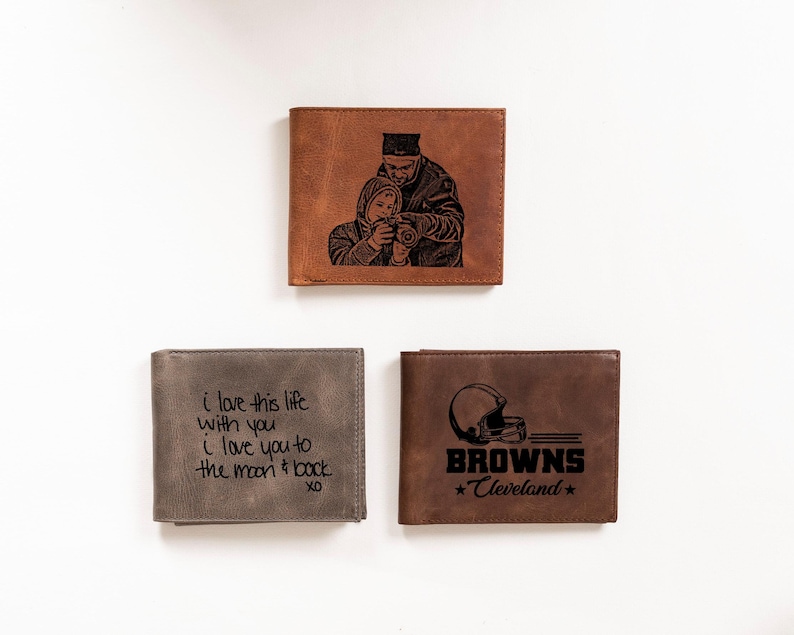 May include: Three different leather wallets with personalized engravings. The first wallet has a photo of a father and son. The second wallet has the text "i love this life with you I love you to the moon & back XO". The third wallet has a football helmet and the text "BROWNS *Cleveland*".