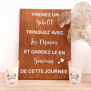 Peut inclure: Panneau en bois avec texte blanc : "PRENEZ UN GOBELET TRINQUEZ AVEC LES MARIÉS ET GARDEZ LE EN SOUVENIR DE CETTE JOURNEE." Deux gobelets en plastique givré avec un dessin de voiture et des noms.