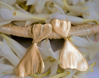 May include: A pair of gold-tone earrings with a heart-shaped design. The earrings are made of metal and have a textured finish.