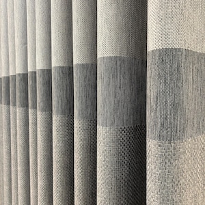Può includere: Un set di tende a tutta altezza caratterizzate da un design plissettato verticale. Il tessuto presenta un motivo a blocchi di colore con bande orizzontali alternate di grigio chiaro, grigio medio e grigio scuro, in una trama tessuta.