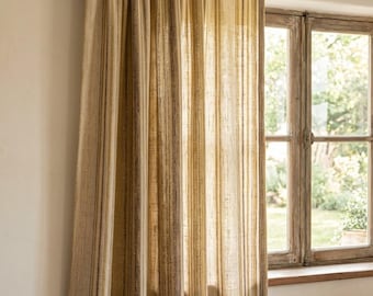May include: A floor-length curtain featuring vertical stripes in shades of beige, tan, and dark brown. The fabric has a textured, woven appearance and hangs from a dark wooden rod mounted on the wall above a window frame.