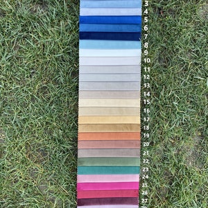 May include: A vertical fabric swatch sample strip featuring thirty-one distinct colour variations of velvet material, arranged in a gradient from light grey to dark blue, beige, earth tones, pinks, greens, and deep purple.