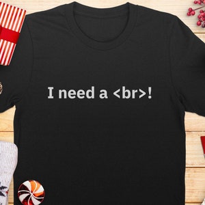 Könnte beinhalten: Schwarzes T-Shirt mit dem Text "I need a <br>!". Das Bild zeigt Weihnachtsdekorationen, darunter ein Geschenk, Ornamente und eine Schneeflocke. Ein Pullover und ein Lutscher sind ebenfalls zu sehen.