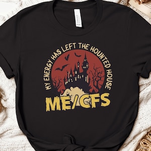 Könnte beinhalten: Ein schwarzes Kurzarm-T-Shirt mit einer Grafik einer Spukhaus-Silhouette vor einem großen roten Mond mit Fledermäusen. Der Text "MY ENERGY HAS LEFT THE HAUNTED HOUSE" steht in einem Bogen darüber und "ME/CFS" in großen gelben Buchstaben darunter.