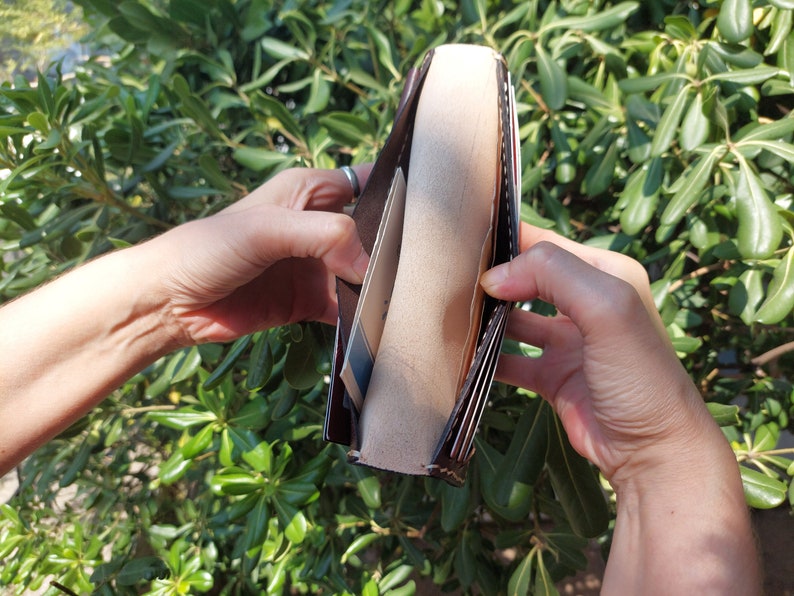 Puede incluir: Una cartera de cuero marr&oacute;n con m&uacute;ltiples ranuras para tarjetas y un portafolios. La cartera est&aacute; abierta y el interior est&aacute; forrado con una tela beige.