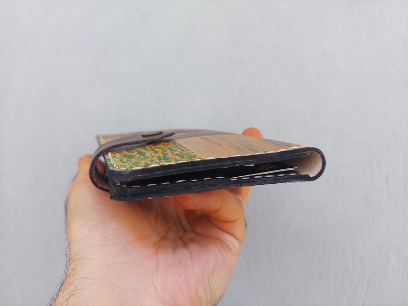 Puede incluir: Una cartera de cuero marr&oacute;n con un dise&ntilde;o estampado multicolor. La cartera est&aacute; doblada por la mitad y tiene un detalle de costura negra.