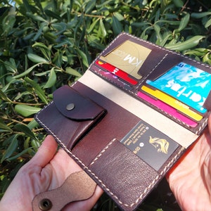 Puede incluir: Una cartera de cuero marr&oacute;n con m&uacute;ltiples ranuras para tarjetas y un bolsillo peque&ntilde;o. La cartera est&aacute; abierta y muestra varias tarjetas en el interior, incluida una tarjeta de cr&eacute;dito con el texto "KM" en ella.