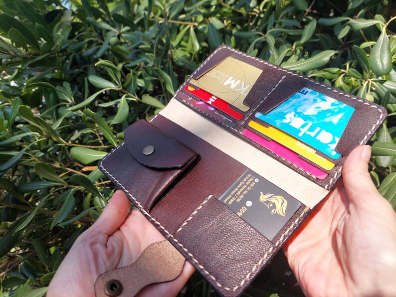 Puede incluir: Una cartera de cuero marr&oacute;n con m&uacute;ltiples ranuras para tarjetas y un bolsillo peque&ntilde;o. La cartera est&aacute; abierta y muestra varias tarjetas en el interior, incluida una tarjeta de cr&eacute;dito con el texto "KM" en ella.