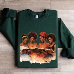 Puede incluir: Una sudadera verde oscuro con una ilustraci&oacute;n de acuarela de cuatro mujeres leyendo libros. Las mujeres est&aacute;n representadas con varios peinados y ropa, con tonos c&aacute;lidos de naranja y marr&oacute;n. La sudadera est&aacute; hecha de un material suave.