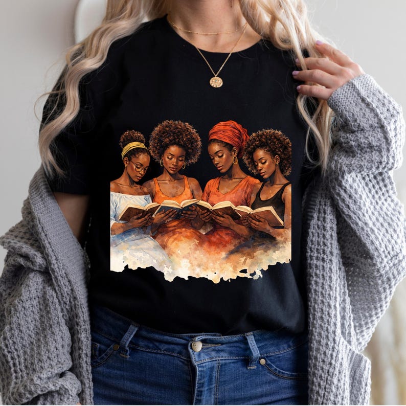 Puede incluir: Camiseta negra con una ilustraci&oacute;n en acuarela de cuatro mujeres leyendo libros. Las mujeres, de piel oscura, visten ropa naranja, amarilla y negra, con tocados. Se ve un collar dorado.