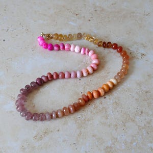 May include: A necklace with a colour gradient, shifting from purple to orange and yellow. The necklace is made of small, rounded beads and has a gold-coloured clasp.