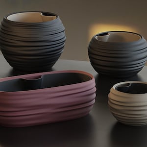 May include: Four decorative ceramic containers in varying sizes and colors. The largest is a dark gray, spherical shape. The second largest is a mauve, oblong shape. The other two are a dark gray and a cream color, both spherical.