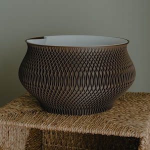 May include: A brown decorative bowl with a unique, patterned exterior. The bowl has a wide, open top with a white interior. The bowl is sitting on a woven, rectangular basket.