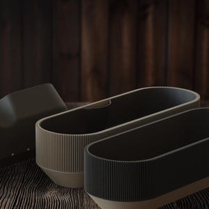May include: Three contemporary planters with a ribbed texture. One is dark grey, another is light grey, and the third is dark brown. The planters have a rounded rectangular shape and sit on a wooden surface.