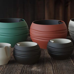 May include: A collection of ceramic bowls in various sizes and colors, including green, red-orange, black, and white. The bowls have a textured, layered design and are arranged on a wooden surface. The interior of the bowls is a contrasting color.