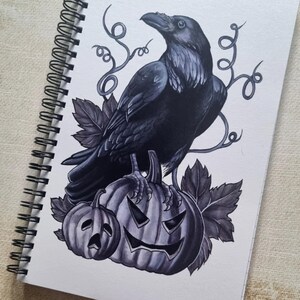 Puede incluir: Un cuervo negro posado sobre una calabaza tallada con una cara espeluznante. El cuervo está rodeado de enredaderas y hojas, creando una escena de Halloween oscura y misteriosa.