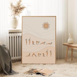 Pode incluir: Uma impressão artística emoldurada com uma ilustração minimalista de uma sequência de ioga. A obra de arte retrata uma série de poses numa paleta de cores quentes, com um sol e uma paisagem estilizada no fundo. A impressão é exibida num tapete branco e fofo.
