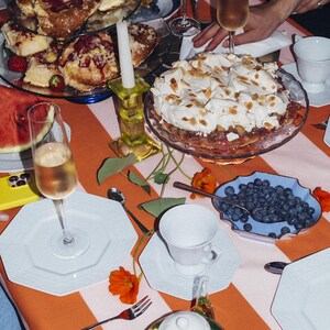 May include: A table set for a celebration, featuring a striped orange and white tablecloth. There are pastries, a cake, blueberries, and tea. Champagne flutes and white plates are also present, creating a celebratory atmosphere.