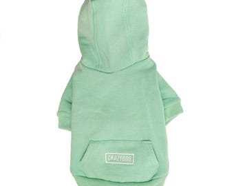 Puede incluir: Una sudadera con capucha de color verde claro para mascotas, con un bolsillo canguro y la palabra "CRAZYBOO" impresa en blanco en el bolsillo.