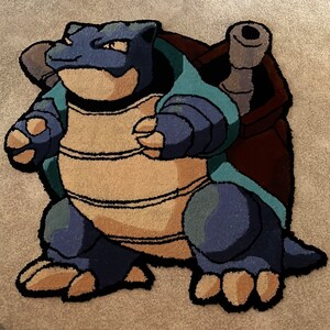 Könnte beinhalten: Ein blauer und brauner Teppich mit einer Comicfigur aus dem Pokemon-Franchise. Die Figur ist eine blaue Schildkröte mit einer braunen Schale und einem breiten, zahnigen Grinsen.