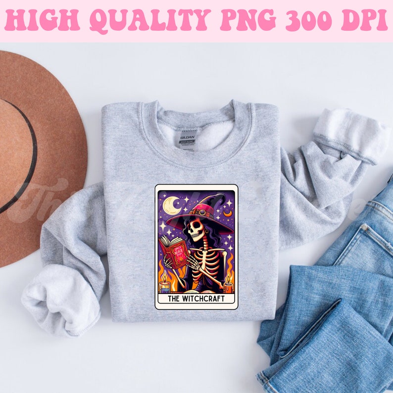K&ouml;nnte beinhalten: Ein graues Sweatshirt mit einem Tarotkarten-Design, das ein Skelett zeigt, das einen Hexenhut tr&auml;gt und ein Buch h&auml;lt. Die Karte lautet "The Witchcraft".
