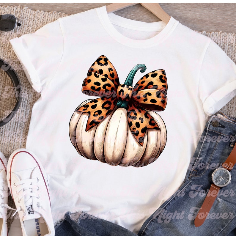 May include: White pumpkin with a large leopard print bow. The pumpkin is a fall themed design for a t-shirt.
