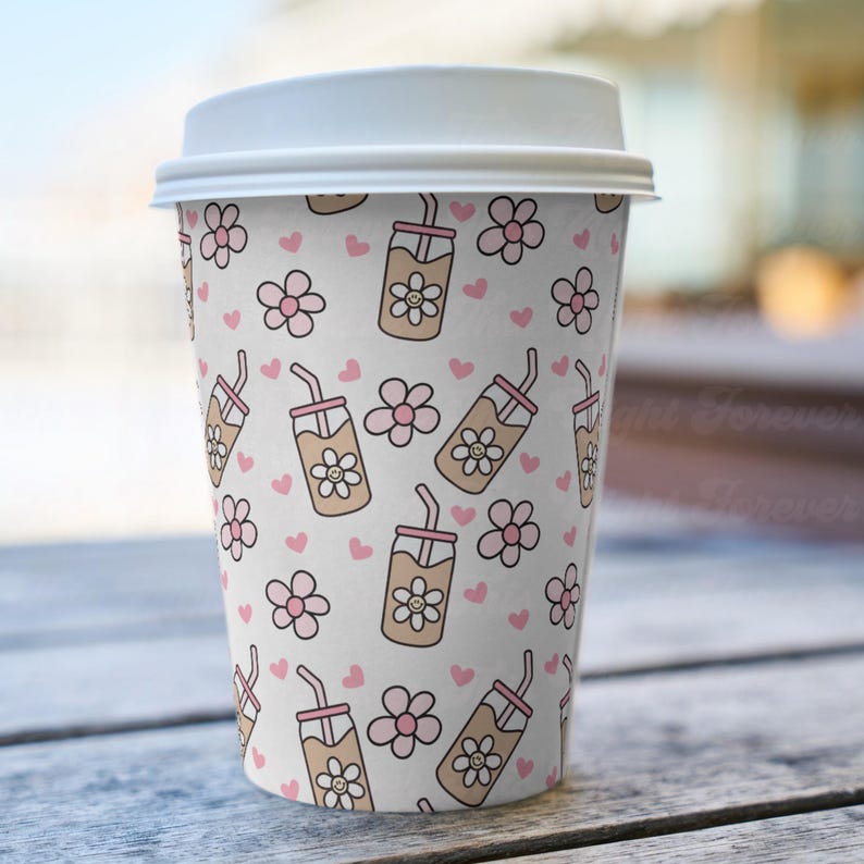 May include: A white paper coffee cup with a white lid. The cup is decorated with a repeating pattern of pink flowers, pink hearts, and brown iced coffee drinks with smiling flower faces.