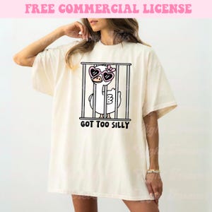 May include: A white t-shirt with a cartoon illustration of a duck wearing heart-shaped sunglasses and a flower in its hair. The duck is in a cage and the text "GOT TOO SILLY" is printed below the image.