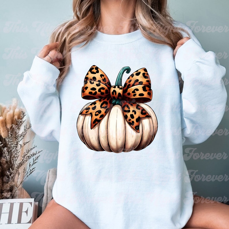 May include: A light blue sweatshirt with a white pumpkin with a brown and orange leopard print bow on top.