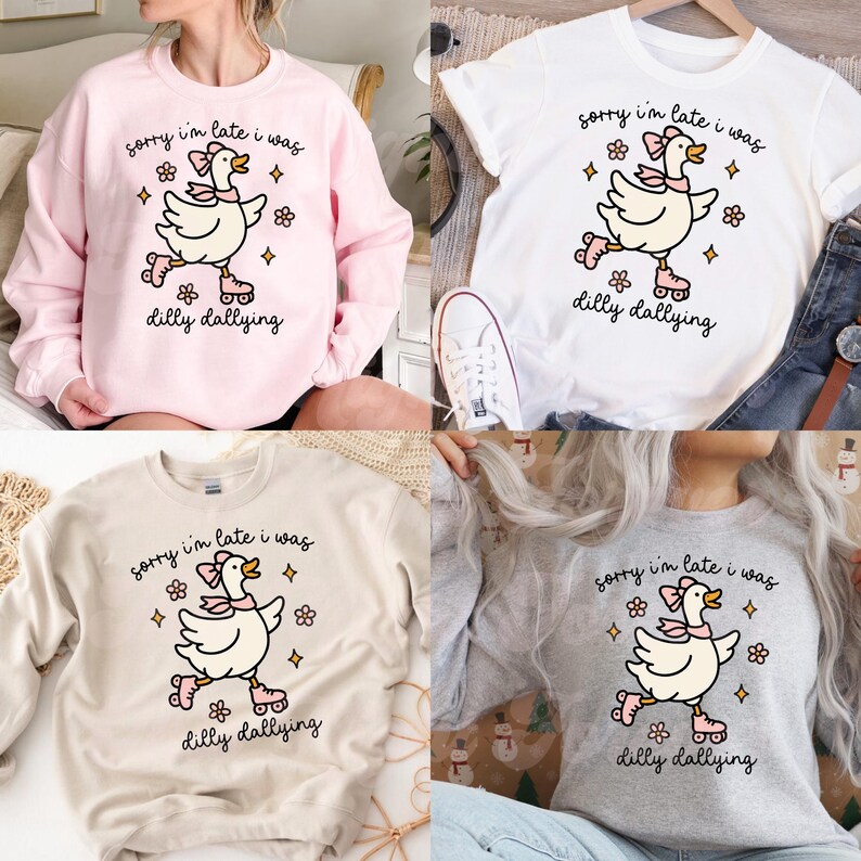K&ouml;nnte beinhalten: Verschiedene Sweatshirts und ein wei&szlig;es T-Shirt mit einer Cartoon-Gans auf Rollschuhen. Die Gans hat eine rosa Schleife und ist von Blumen- und Sterngrafiken umgeben. Der Text "sorry I'm late I was dilly dallying" ist aufgedruckt.