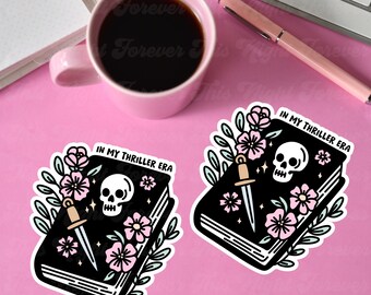 May include: Two black and white stickers with a book, a dagger, a skull, and pink flowers. The text on the stickers reads "In My Thriller Era".