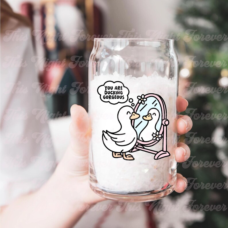 K&ouml;nnte beinhalten: Ein durchsichtiges Glas mit einem rosafarbenen und wei&szlig;en Cartoon-Enten-Design. Die Ente schaut in einen Spiegel und der Text "You are ducking gorgeous" befindet sich in einer Gedankenblase &uuml;ber der Ente.