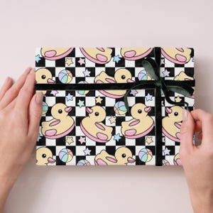 May include: Gift-wrapped present featuring a repeating pattern of yellow rubber ducks, beach balls, and stars on a black and white checkered background. The gift is tied with a dark green ribbon.