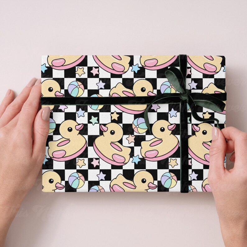 May include: Gift-wrapped present featuring a repeating pattern of yellow rubber ducks, beach balls, and stars on a black and white checkered background. The gift is tied with a dark green ribbon.