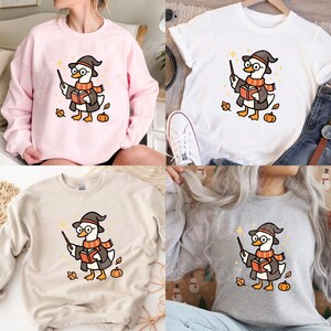 May include: Four different tops: a pink sweatshirt, a white t-shirt, a beige sweatshirt, and a gray sweatshirt. Each features a cartoon duck wearing a wizard hat, glasses, and a scarf, holding a wand and a book, with autumn leaves and pumpkins.