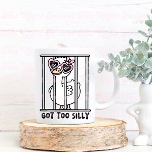 May include: White ceramic mug with a cartoon illustration of a goose wearing pink heart-shaped sunglasses and a pink bow, inside a cage. The text "GOT TOO SILLY" is printed below the image.