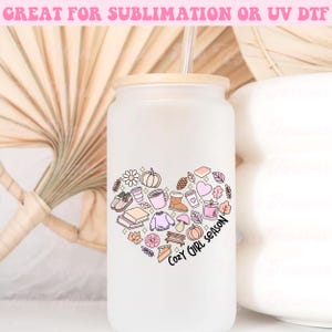 Op de afbeelding: Een witte, gematteerde glazen beker met een houten deksel en een rietje. De beker heeft een roze hartontwerp met herfstthema-illustraties en de tekst "Cozy Girl Season".
