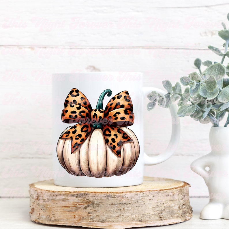 May include: White ceramic mug with a hand-painted design of a white pumpkin with a brown and orange leopard print bow. The pumpkin has a green stem.