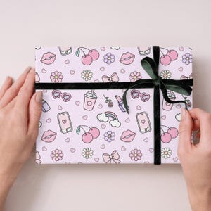 May include: Pink and white gift wrap with a repeating pattern of cherries, lips, hearts, flowers, rainbows, cell phones, sunglasses, and lipstick. The gift is wrapped with a black ribbon.