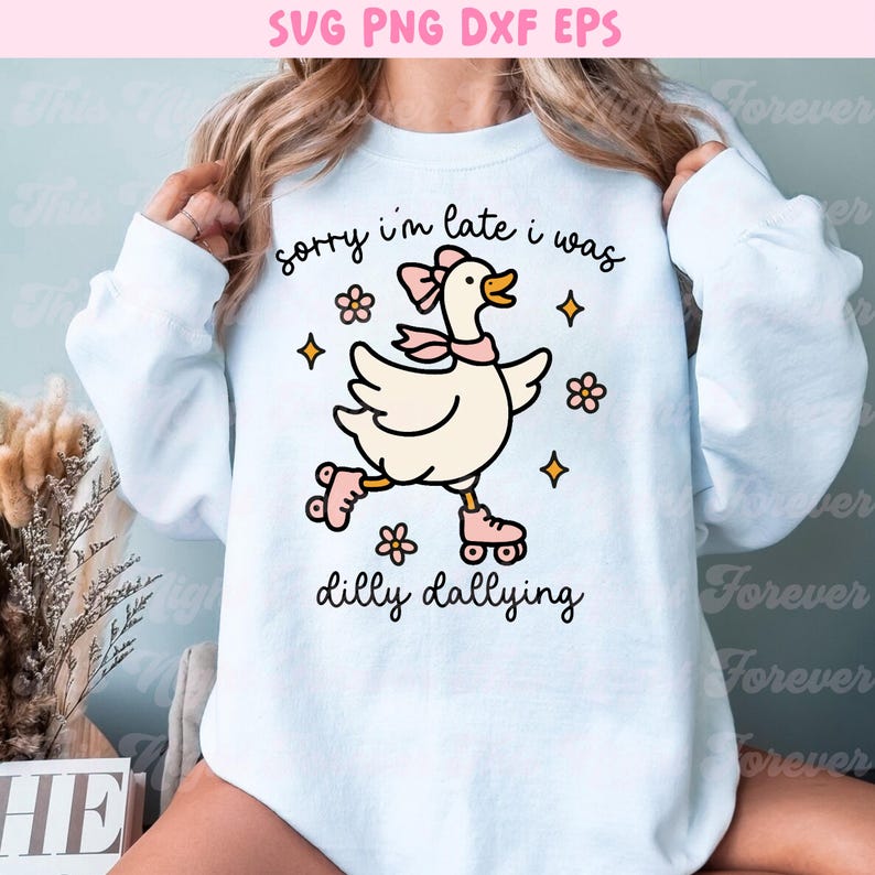 K&ouml;nnte beinhalten: Wei&szlig;es Sweatshirt mit einer Cartoon-Gans auf Rollschuhen, mit rosa Schleife und Schal. Der Text "sorry i'm late i was dilly dallying" ist in schwarzer Schrift geschrieben. Blumen- und Sterngrafiken umgeben die Gans.