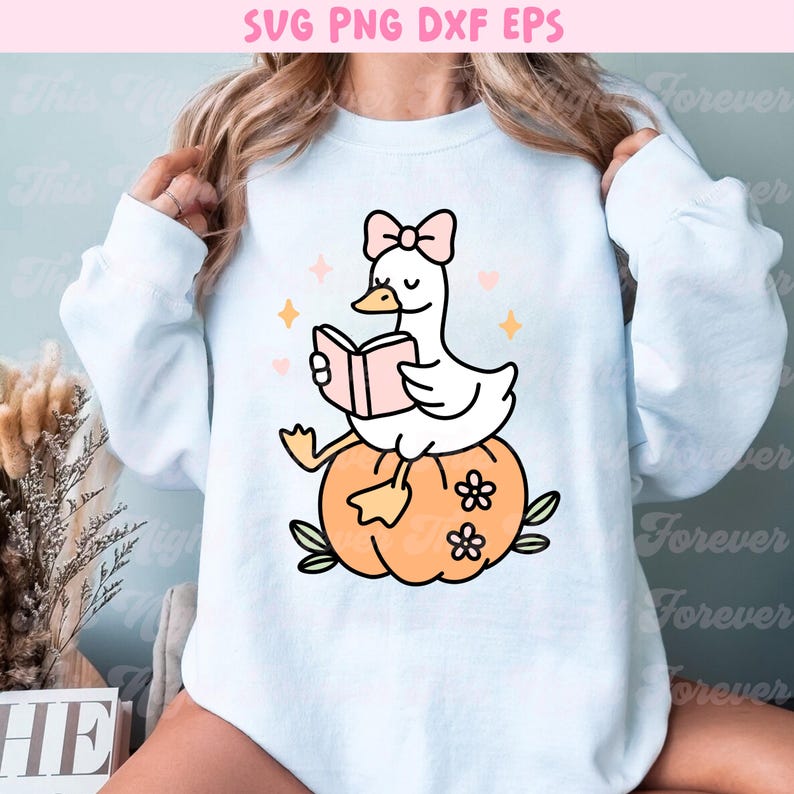 May include: White sweatshirt with a cartoon illustration of a white goose wearing a pink bow and reading a pink book while sitting on an orange pumpkin. The image includes the text "SVG PNG DXF EPS".