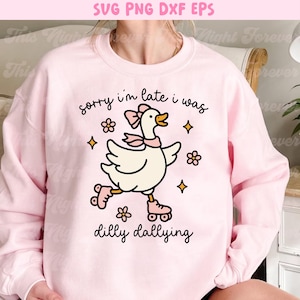 K&ouml;nnte beinhalten: Hellrosa Sweatshirt mit einem Cartoon-Gans auf Rollschuhen, mit dem Text "sorry i'm late i was dilly dallying". Das Design beinhaltet Blumen und Sterne.