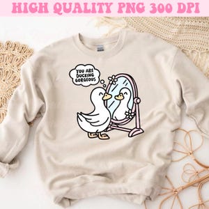 K&ouml;nnte beinhalten: Ein beiger Pullover mit einem Aufdruck eines Entchens, das in einen Spiegel schaut. Die Gedankenblase &uuml;ber dem Entchen sagt "You are ducking gorgeous".