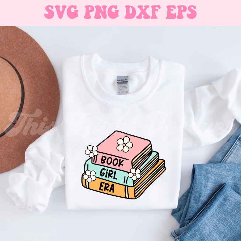 May include: A white sweatshirt with a stack of three books with the text "Book Girl Era" on the front. The books are pink, blue, and yellow with white flowers on the top book.