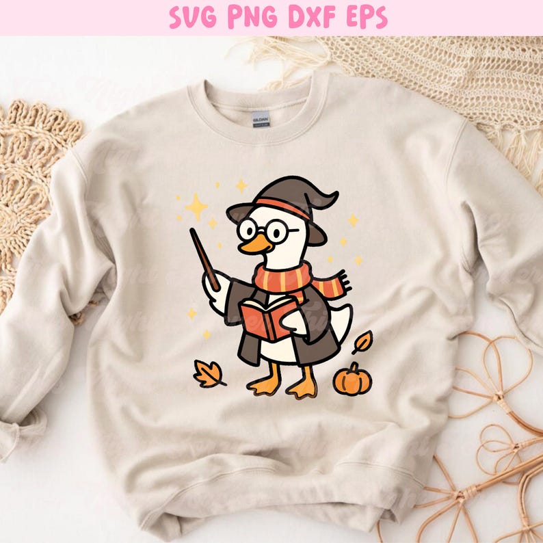 May include: Beige sweatshirt featuring a cartoon duck dressed as a wizard, wearing a hat, glasses, and a scarf. The duck holds a wand and a book, with stars, a pumpkin, and a leaf. Text at the top reads "SVG PNG DXF EPS".