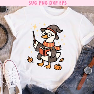 May include: White t-shirt featuring a cartoon goose dressed as a wizard, wearing a hat, scarf, and glasses, holding a wand and book. The design includes stars, leaves, and a pumpkin. Text at the top reads "SVG PNG DXF EPS".