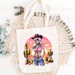 May include: Off-white canvas tote bag featuring a colorful illustration of a skeleton cowgirl wearing a hat and sunglasses, set against a desert sunset with cacti. The design includes a pink top and blue jeans.